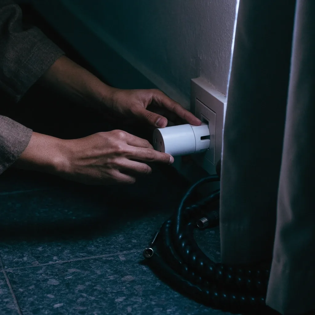Manos colocando un enchufe inteligente en una toma de pared cerca del piso, de noche