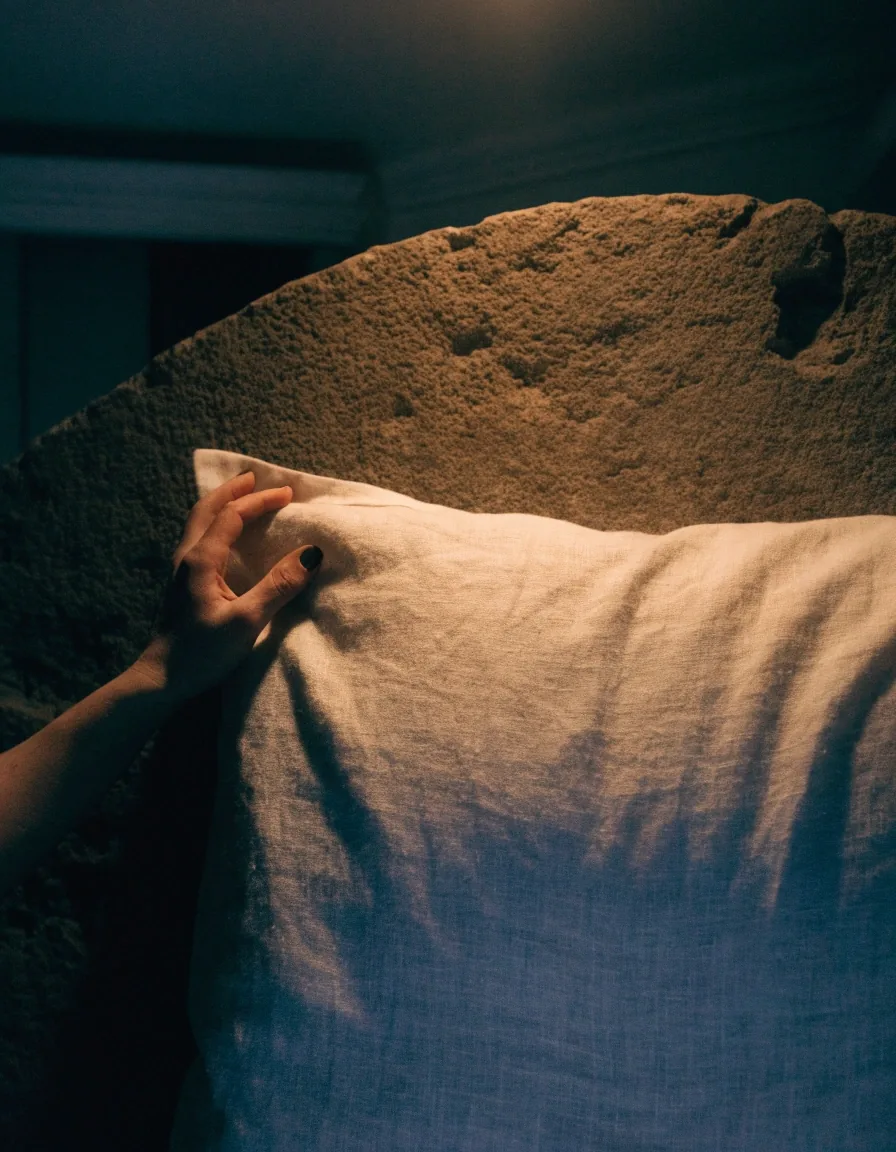 Almohadón decorativo de lino apoyado contra una pared de piedra oscura